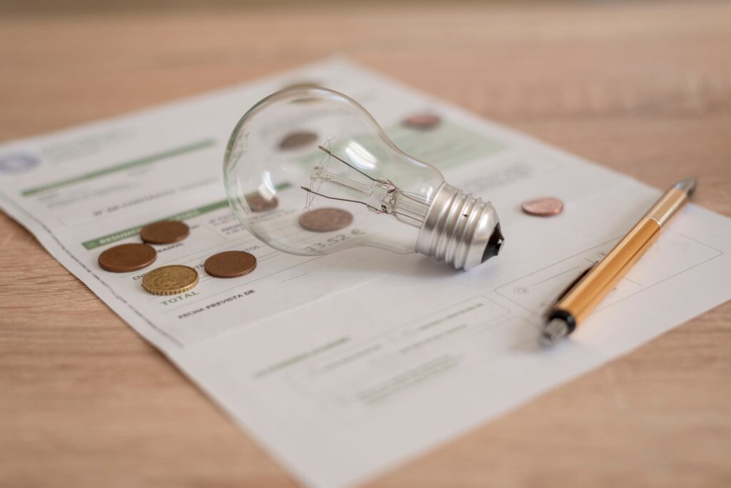 Electricity bill with light bulb, several coins and pen on the desk. Concept of electricity prices