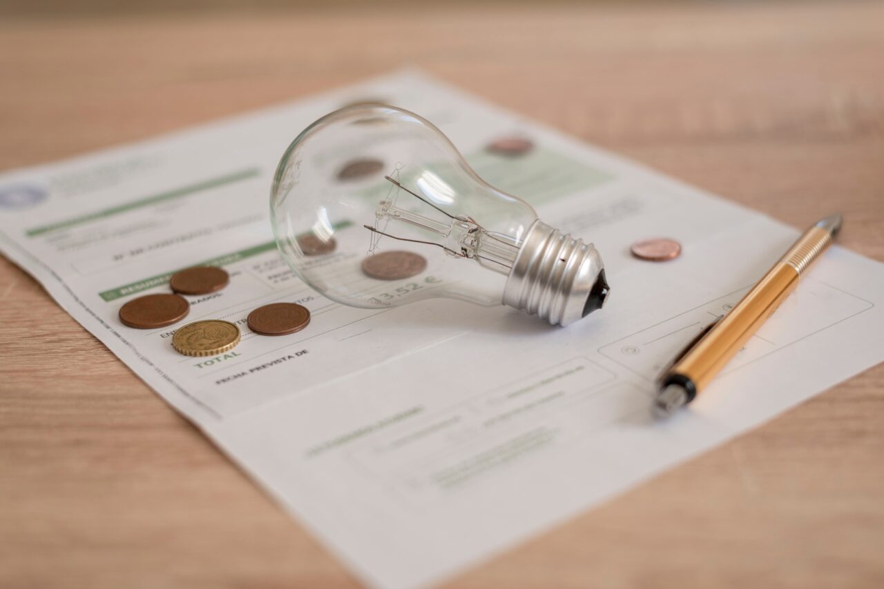 Electricity bill with light bulb, several coins and pen on the desk. Concept of electricity prices