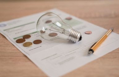 Electricity bill with light bulb, several coins and pen on the desk. Concept of electricity prices
